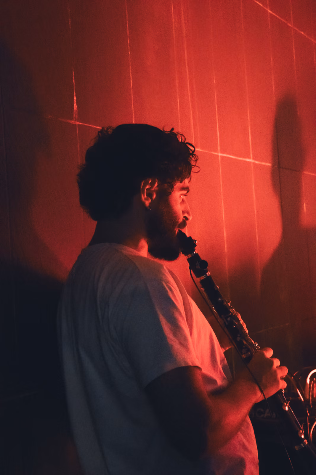 Un musicista con i capelli ricci suona un clarinetto, ripreso di profilo in una luce rossa.